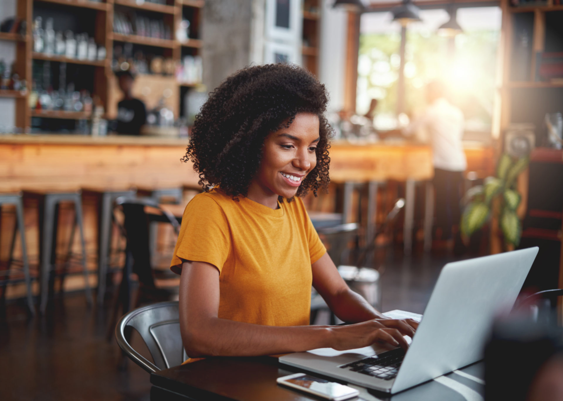 Young african woman professional sitting in cafe typing on laptop emailing hiring manager to follow up after an interview
