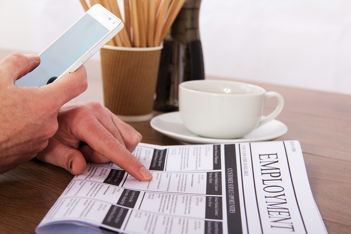 Professional pointing at employment opportunities in a newspaper and holding their cellphone