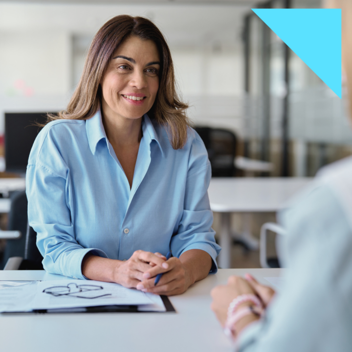 Professional woman conducting a direct hire job interview across a desk in a modern office, reviewing a candidate's resume during a hiring process