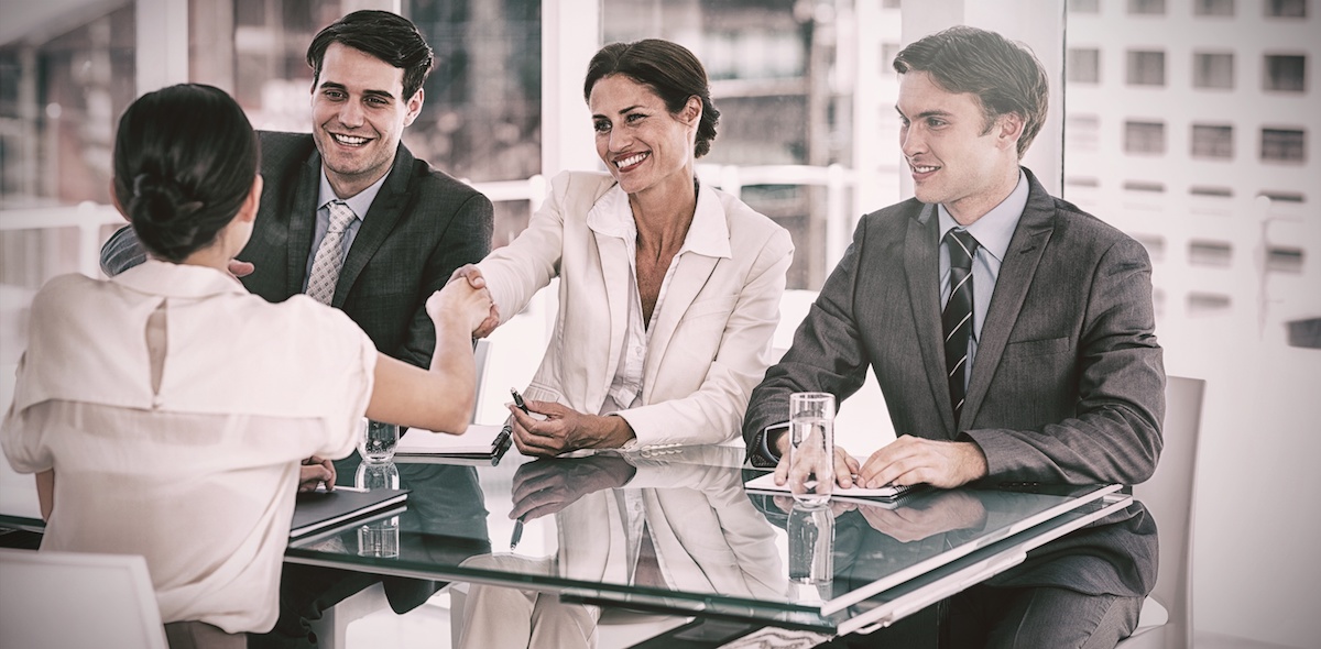Female sitting across the table from three professionals and shaking their hands