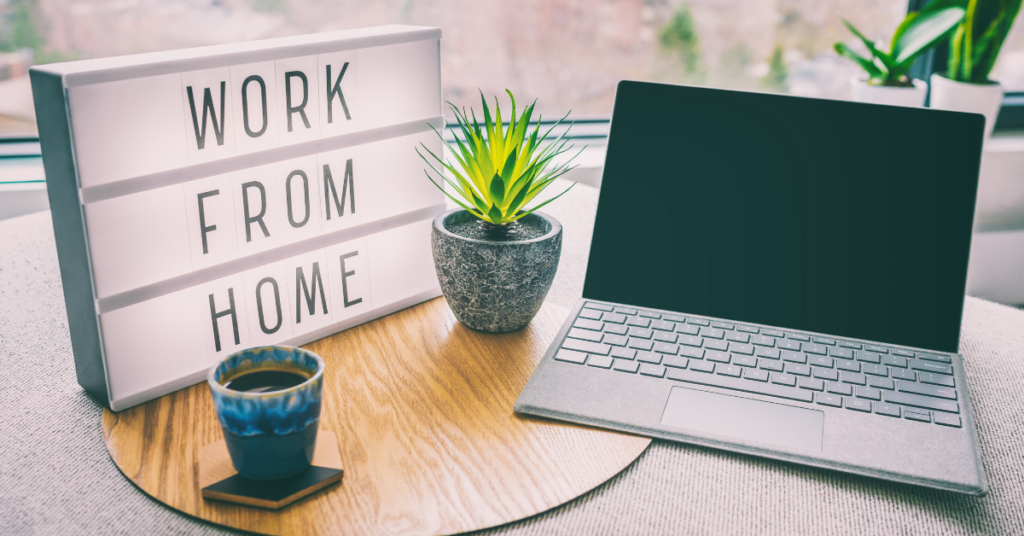 "Work From Home" spelled out on a light up board next to a laptop and a plant