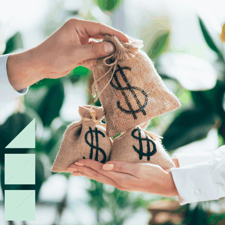 Close-up of two people exchanging small burlap money bags with dollar signs printed on them, symbolizing salary.