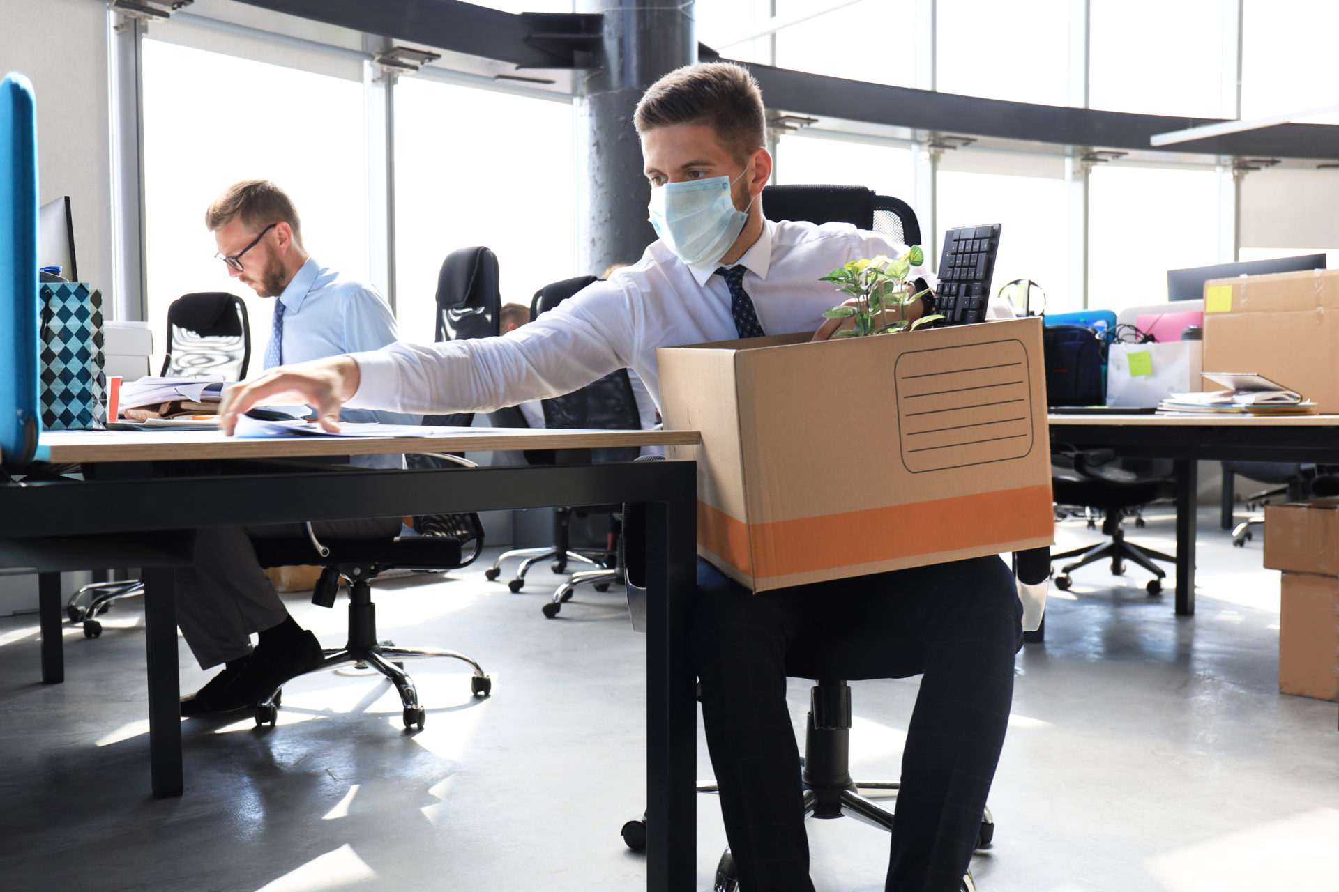 Male employee wearing a mask and clearing off his desk, putting things into a box