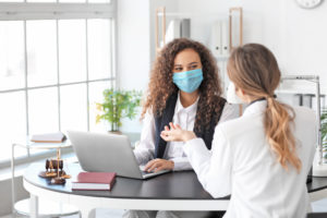 Two females wearing masks and talking in an office