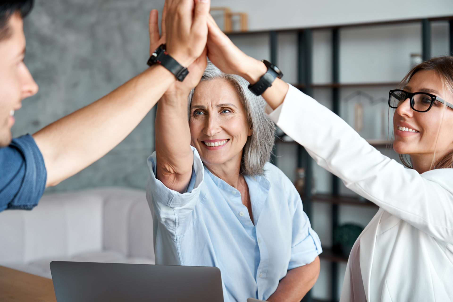 Elderly female high-fiving a young male and female professional in the workplace