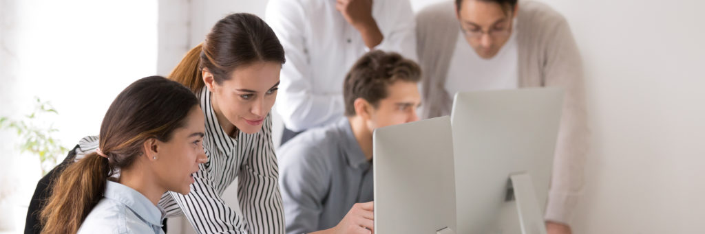 Female workplace mentor pointing to an intern's computer screen, helping her with a task