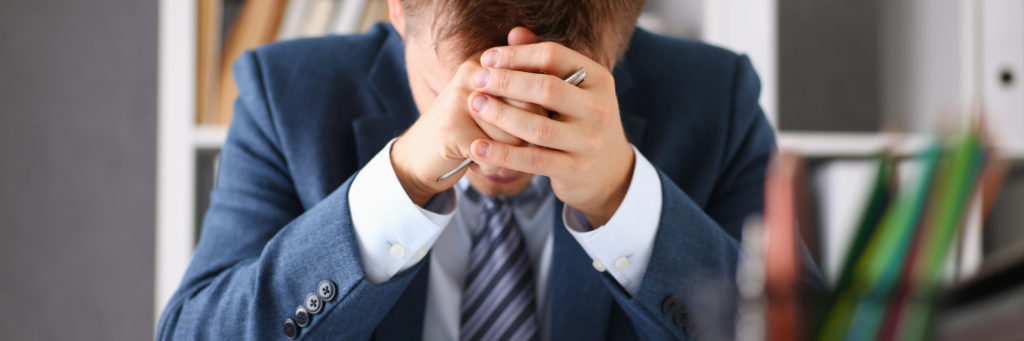 Man at his desk covering his face with his hands as he is experiencing stress