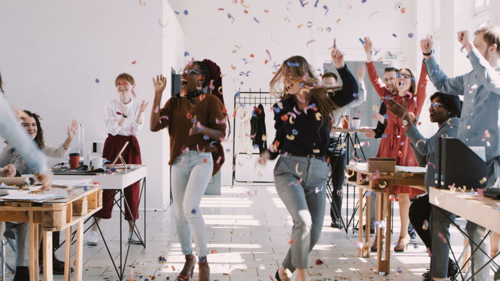 Colleagues celebrate success with team by throwing confetti in the office