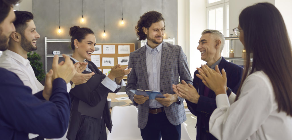Team of smiling professionals clapping and congratulating coworker for a job well done