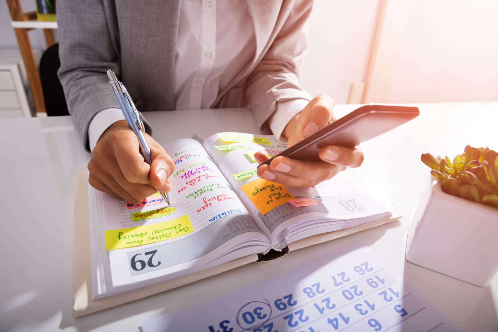 Professional sitting at desk holding a mobile phone while writing in their planner