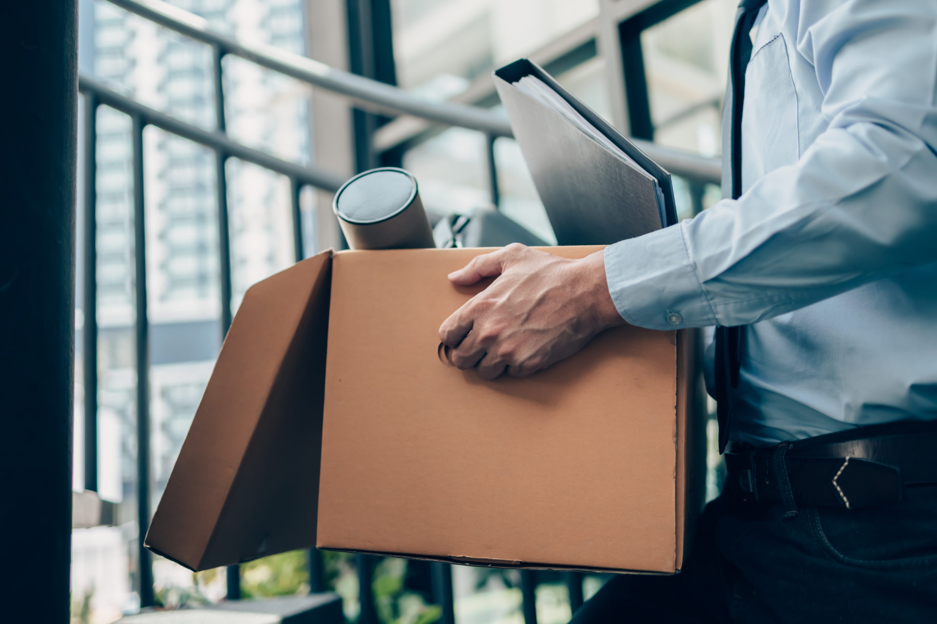 Businessman leaving a job, holding cardboard box and laptop bag, dossier and drawing tube in box.