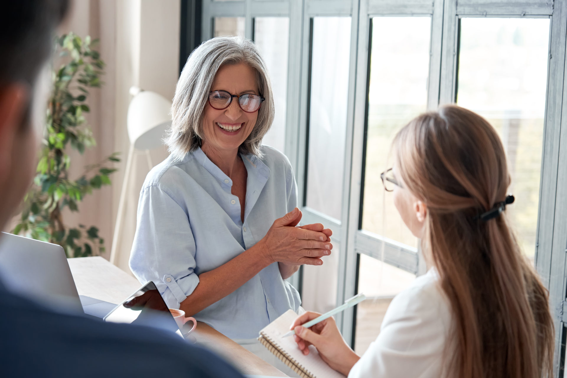 Seasoned Female professional mentoring a female apprentice; apprentice is listening while taking notes inside an office.