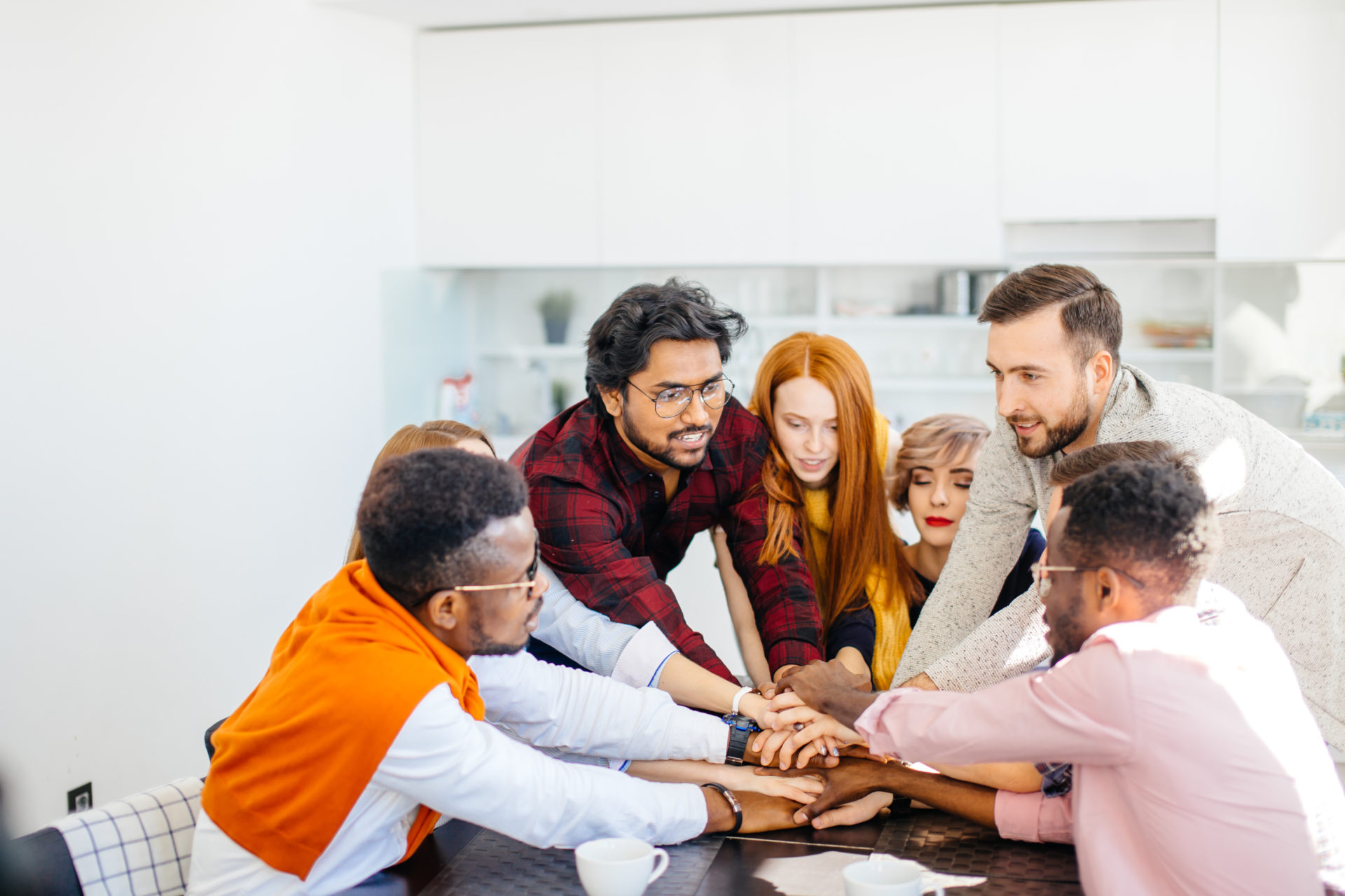 Diverse professionals standing up around a table stacking their hands together