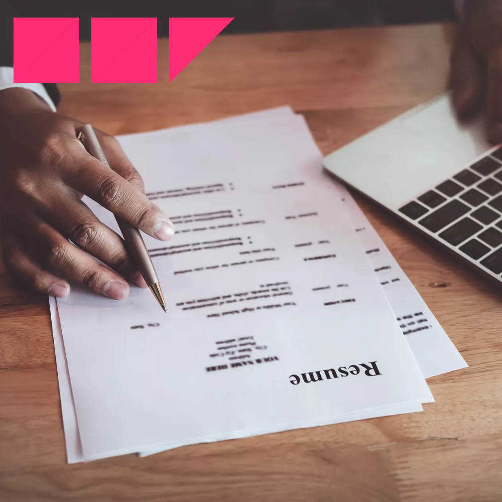 Job seeker updating a resume on a laptop while reviewing a printed copy, focusing on adding the right keywords from the job description to improve their chances of getting noticed.