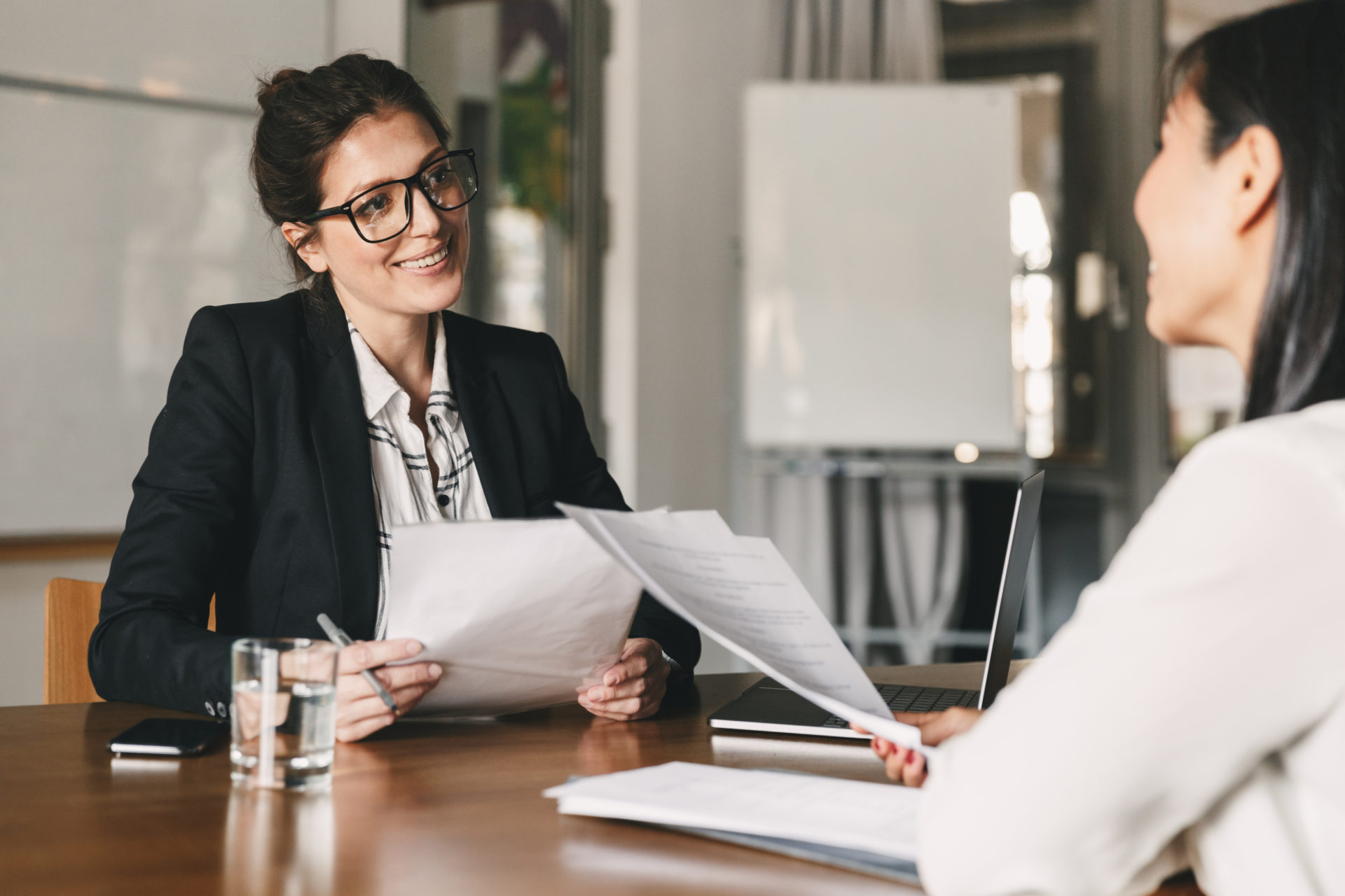 Smiling businesswoman holding resume and talking to female leadership candidate during a job interview