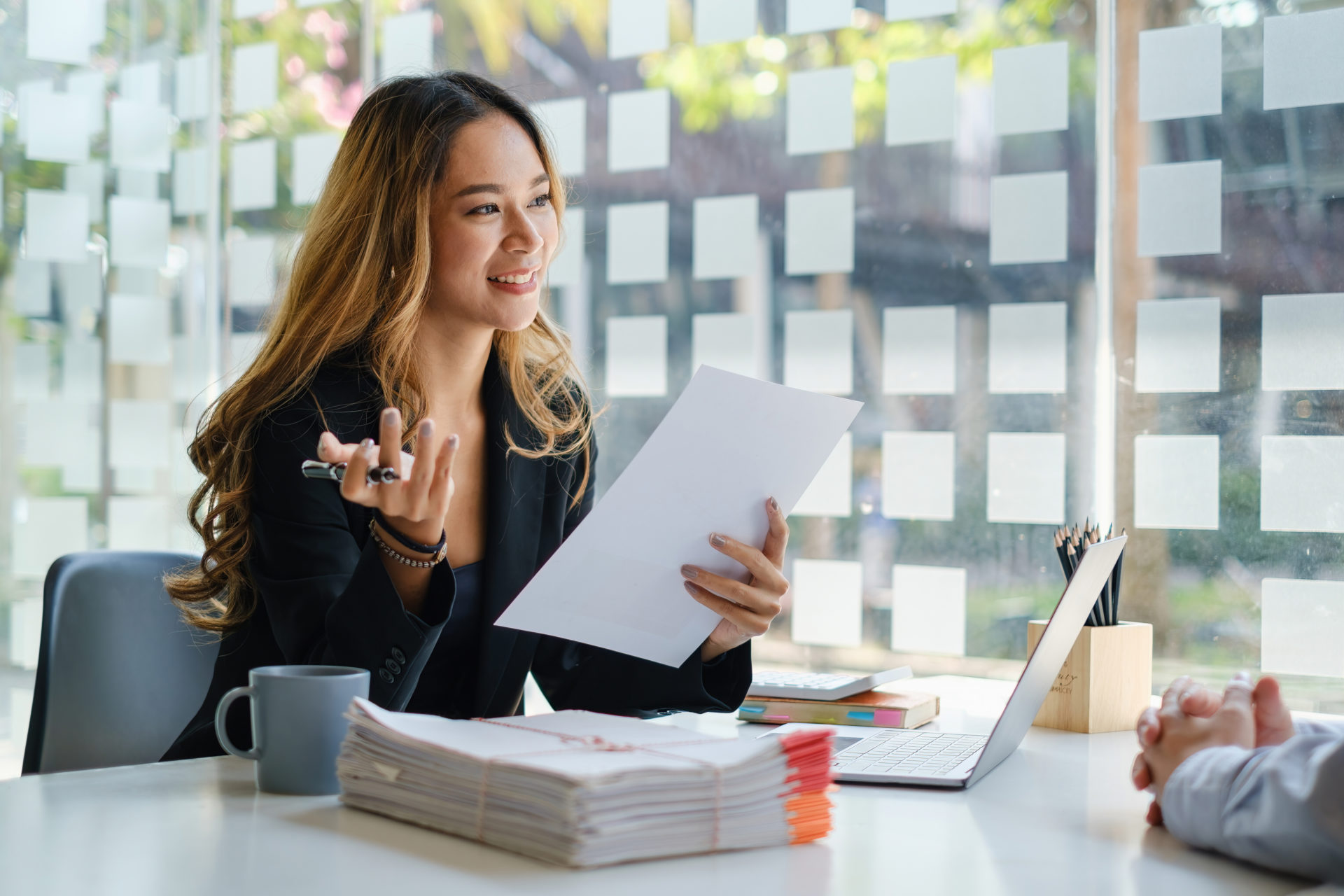 Female hiring manager conducting a skill based interview at her desk with a stack of hiring assessments