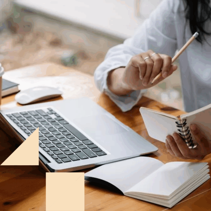 Female professional at her desk with her laptop open conducting research on a company while holding a notebook and a pencil