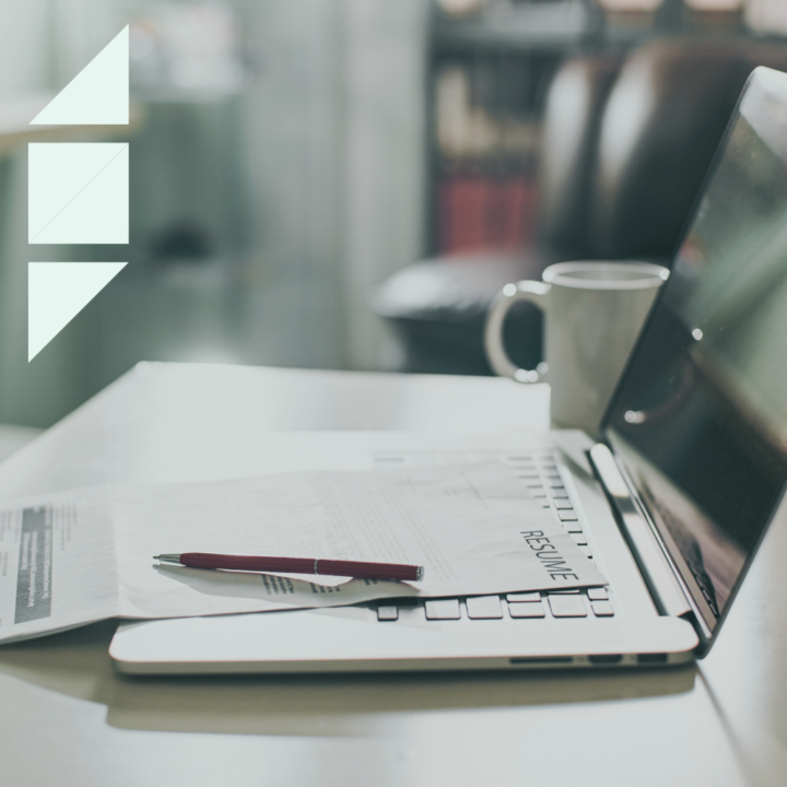 A graduate school resume placed on a laptop keyboard with a pen resting on top. A coffee mug sits nearby on the desk in a softly lit study or office setting, creating a focused and professional atmosphere.