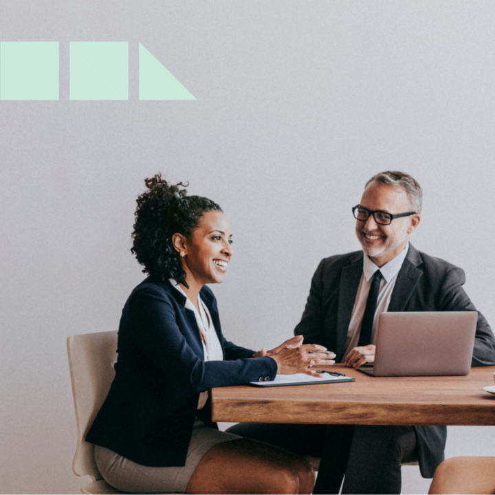 Two people operations employees sitting at a desk with a laptop open brainstorming