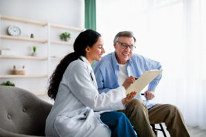 Female insurance nurse showing elderly male patient policy options on a notebook