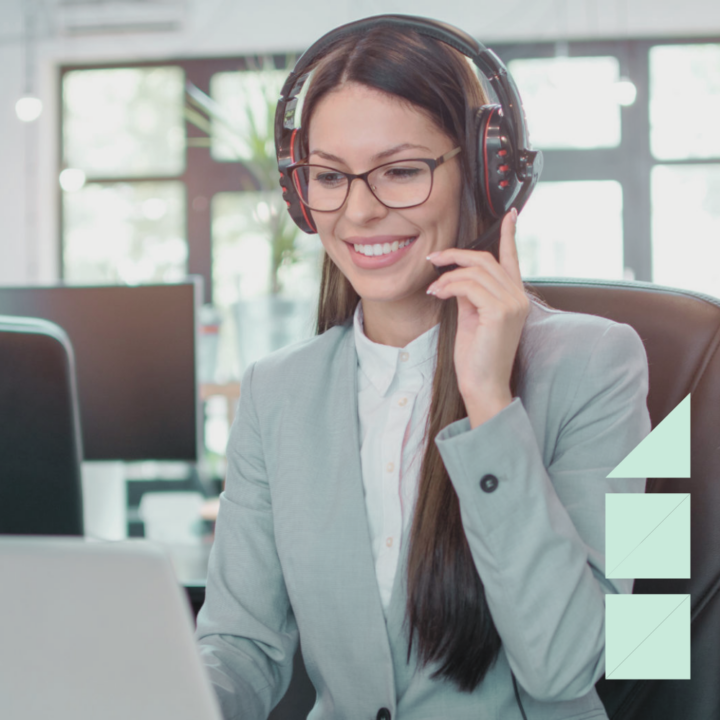 Young successful recruiter wearing gray pantsuit with headset working on laptop in modern office.
