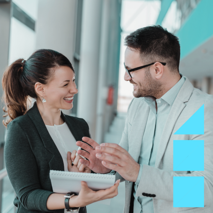 Two human resources professionals dressed in suits smiling while gesturing with their hands and looking at a pad of paper