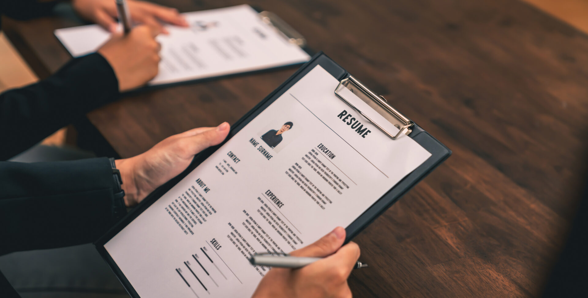 Hiring manager reviewing a candidate's resume on a clipboard at her work desk.