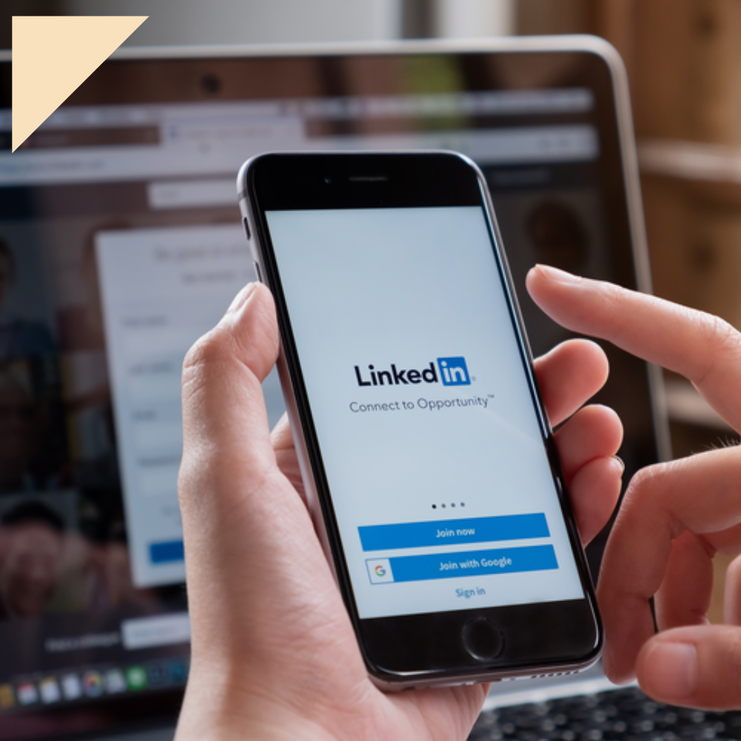 Professional opening up the LinkedIn app on phone while laptop displays their profile
