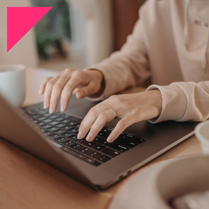 Female Recruiter typing on laptop trying to find different hiring tools sitting at a desk with a mug next to her.