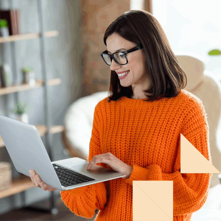 Confident hiring manager in an orange sweater reviewing resumes and candidate profiles on her laptop, exploring strategies for attracting passive candidates in a modern office setting.