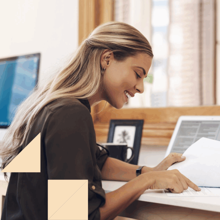 HR professional looking at paperwork at her desk at work with her laptop open conducting preboarding
