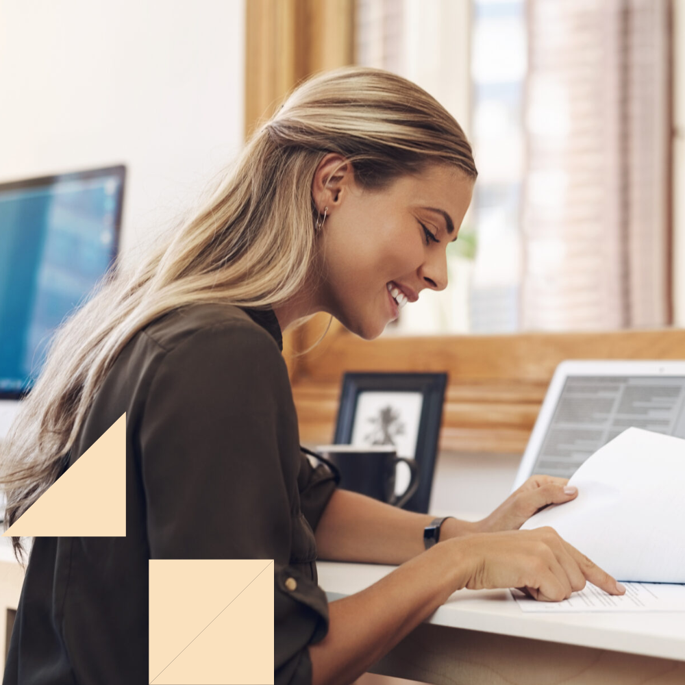 HR professional looking at paperwork at her desk at work with her laptop open conducting preboarding