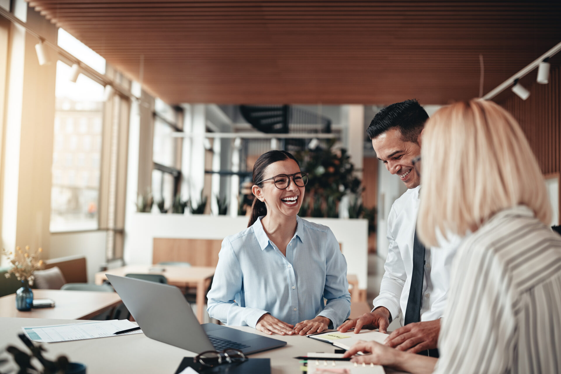 temporary and permanent employees around a desk in an office laughing and communicating about a project they are working on