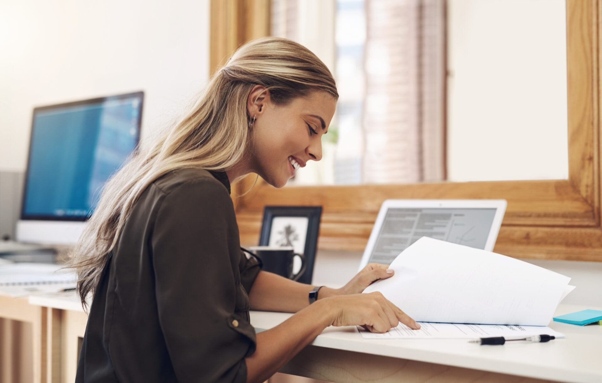 HR professional looking at paperwork at her desk at work with her laptop open conducting preboarding