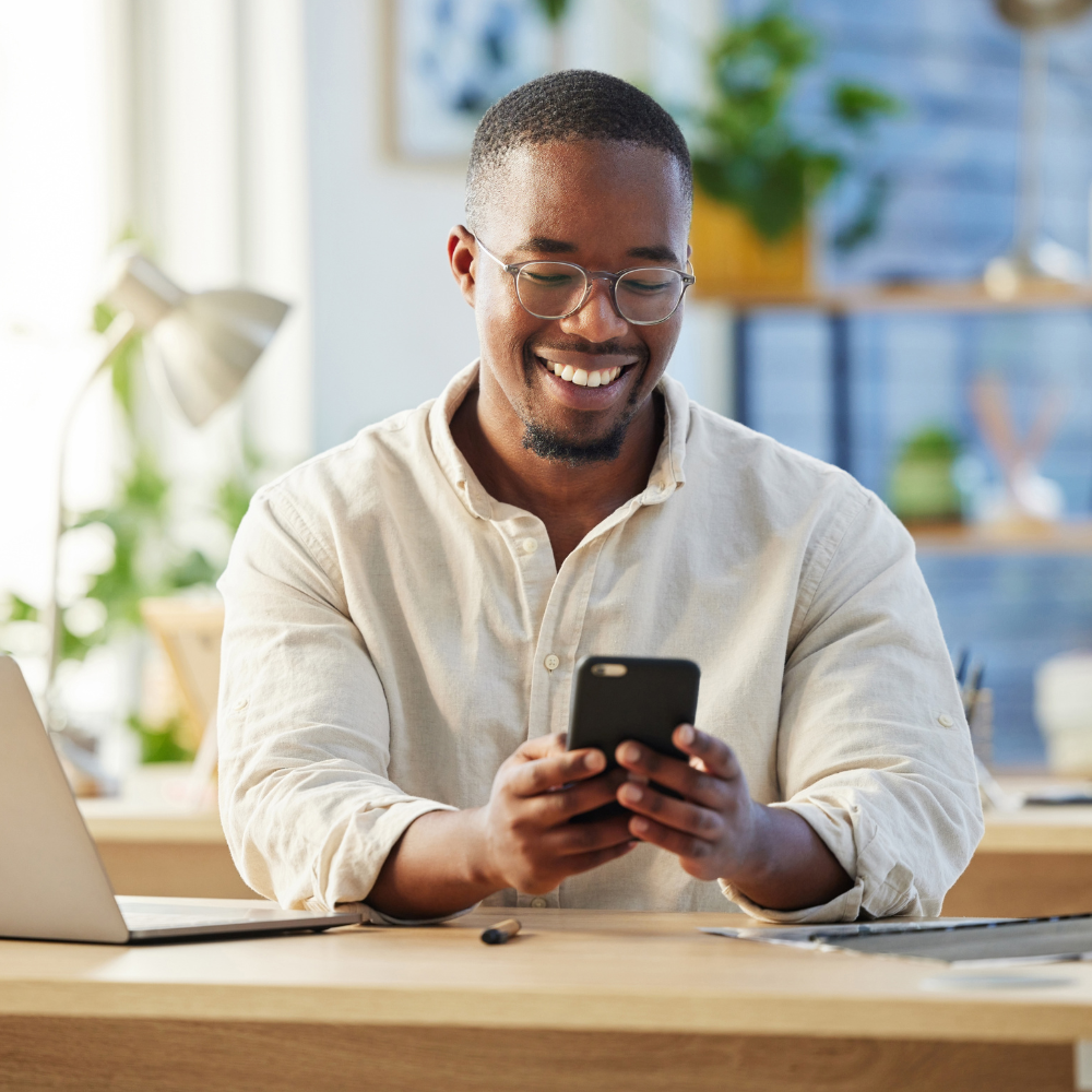 Smiling recruiter sitting at a desk using a smartphone, illustrating the convenience and flexibility of mobile recruiting in a modern workspace.