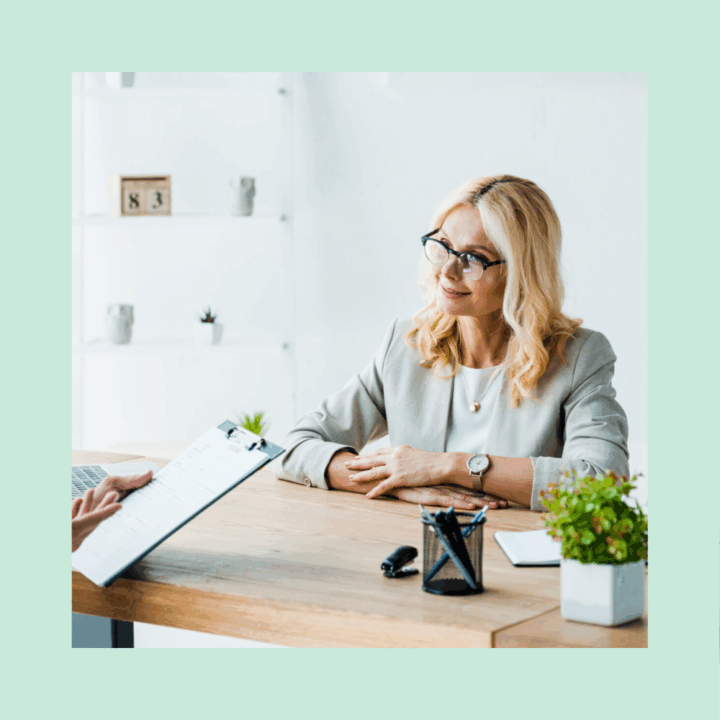 Woman recruiter folding her hands at a desk talking to a male candidate holding a clipboard