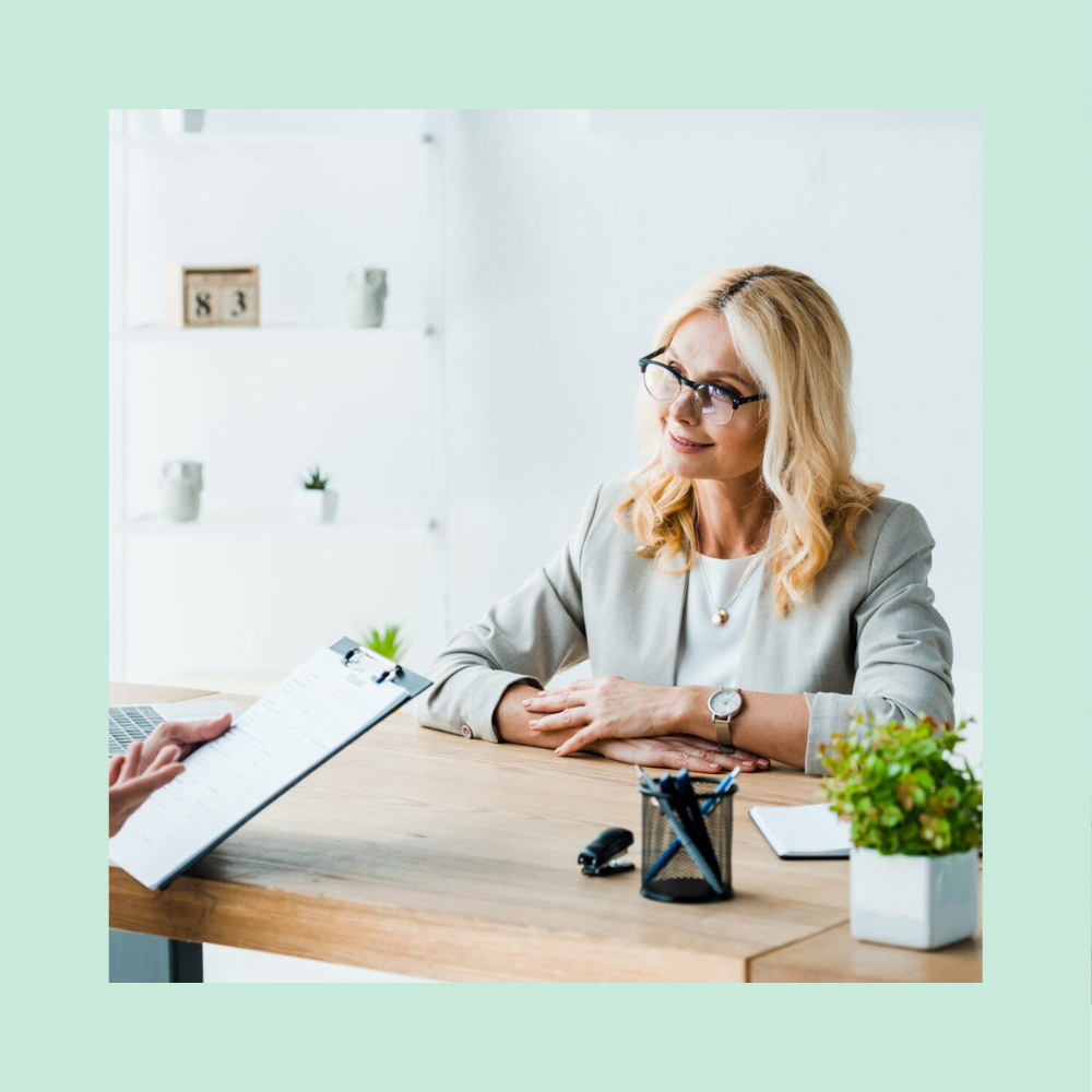 Woman recruiter folding her hands at a desk talking to a male candidate holding a clipboard