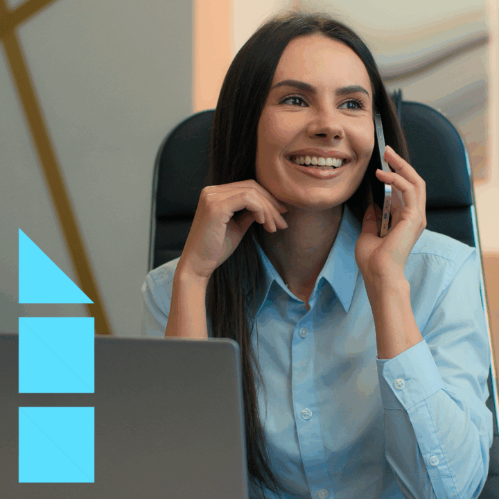 Recruiter smiling while talking on the phone with a candidate at her desk, working on a laptop in a modern office setting, representing professional staffing and hiring services.