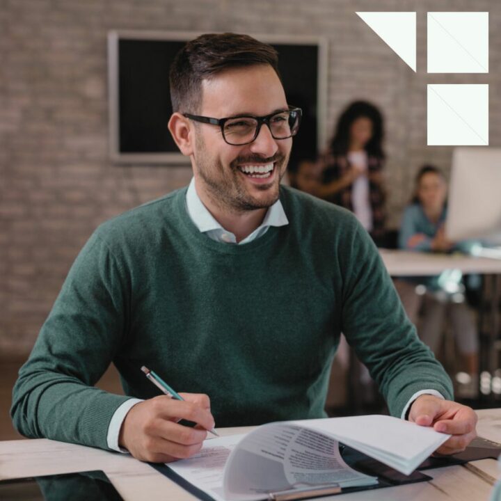 Hiring manager smiling sitting at a desk in front of a job candidate writing on his interview score card with a pen