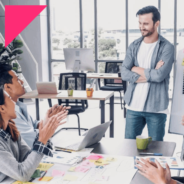 Manager mapping out an employer branding strategy on white board with sticky notes and four employees discussing and clapping sitting around a table