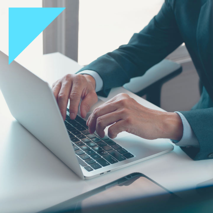 Close-up of a professional in a suit typing on a laptop at a modern office desk. The setting suggests a business or corporate environment, with a smartphone placed nearby.