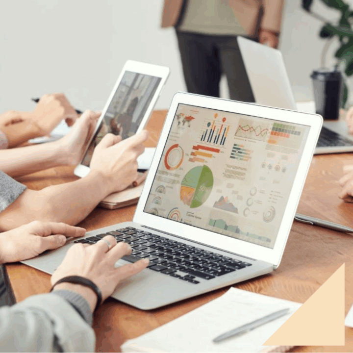 Five professionals with laptop open doing a skill gap analysis sitting around a rectangle wooden desk