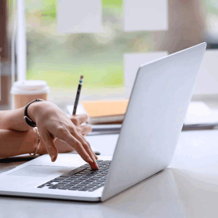 Female typing up a cover letter on her laptop sitting at her desk with a pencil in her hand.