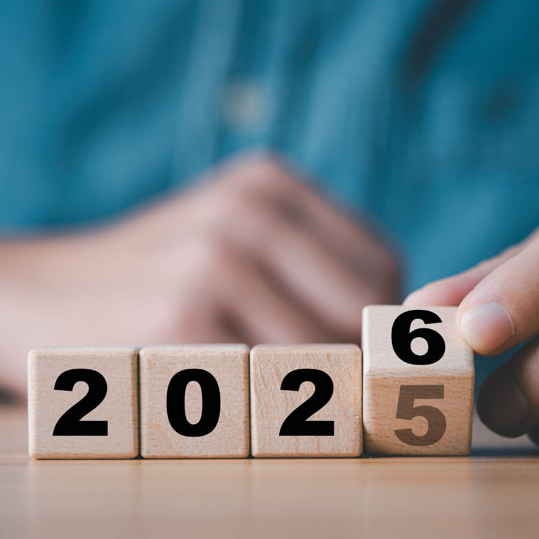 Close-up of a hand flipping a wooden block from “5” to “6,” changing the year from 2025 to 2026, with blurred hands in the background.