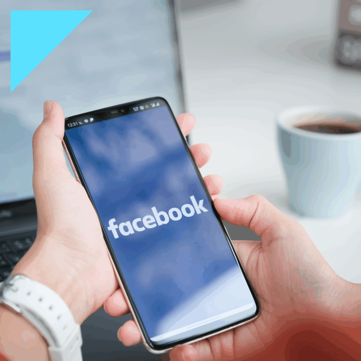 Person using the Facebook app on a mobile phone in a modern workspace with a laptop and coffee, highlighting social media as a tool for recruiting