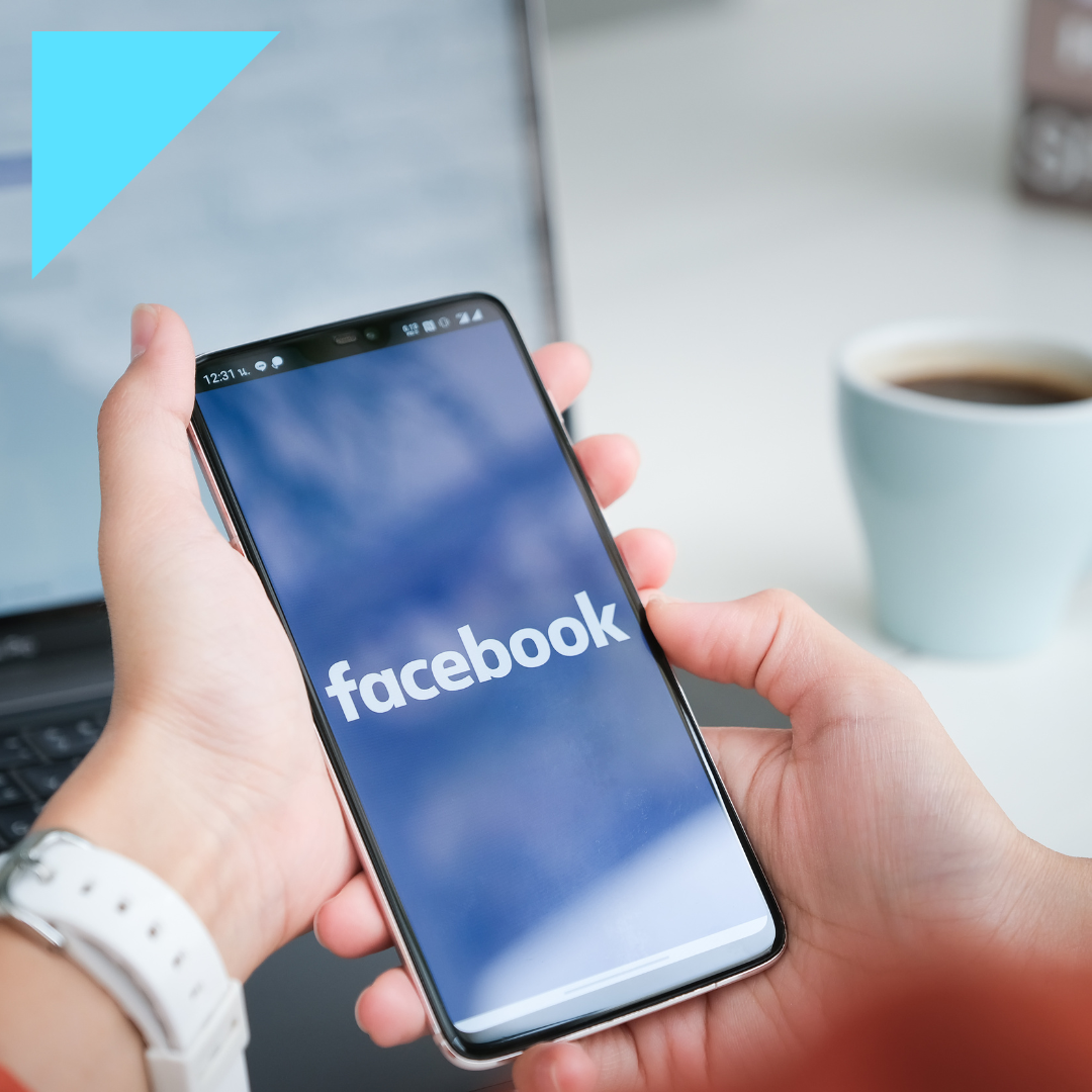 Person using the Facebook app on a mobile phone in a modern workspace with a laptop and coffee, highlighting social media as a tool for recruiting