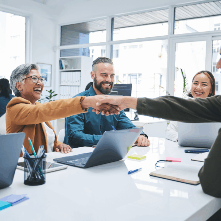 A diverse team of professionals smiling and shaking hands during a successful meeting in a bright modern office, symbolizing collaboration and a positive hiring experience.