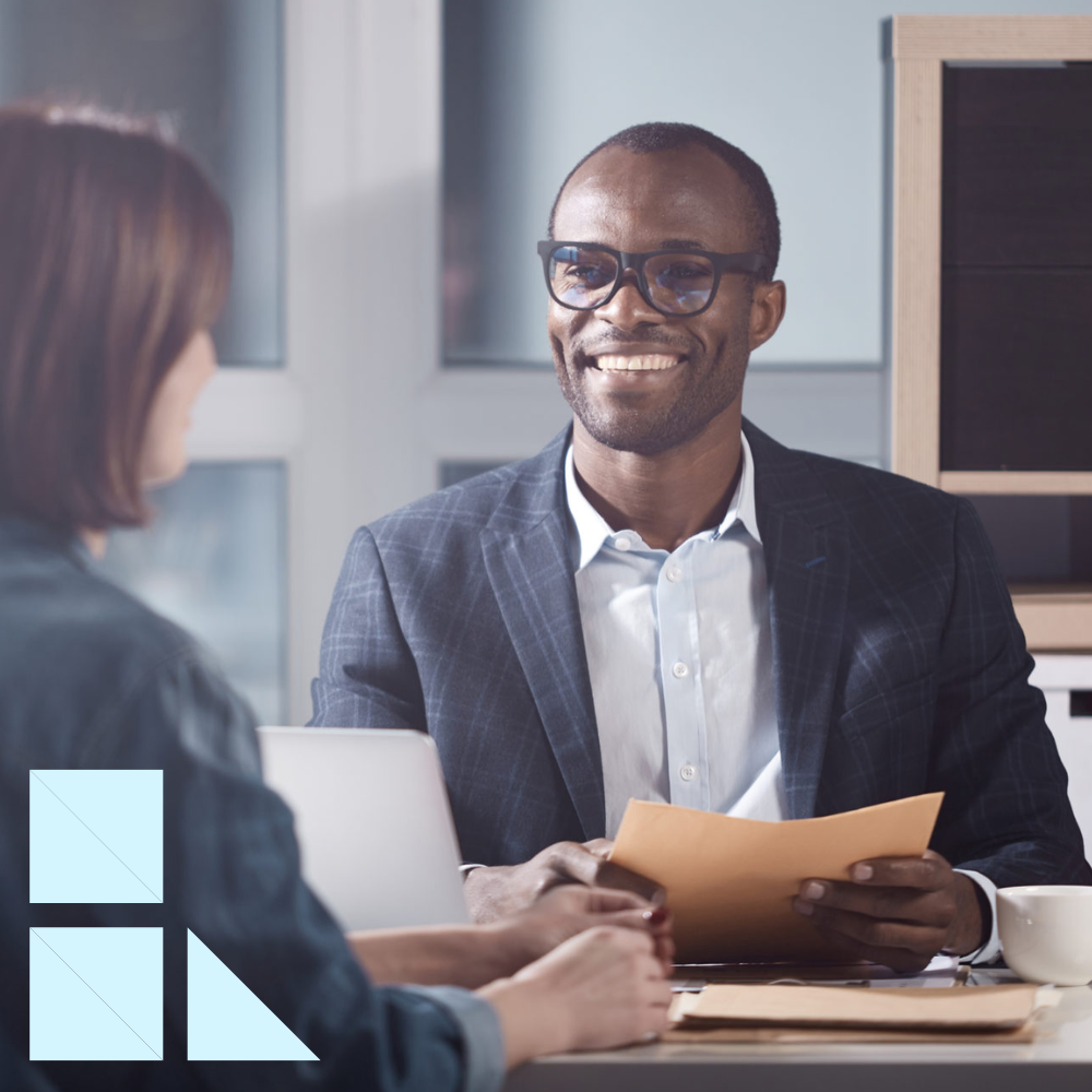 Male hiring manager sitting across from female IT candidate holding her resume conducting an interview in a modern office