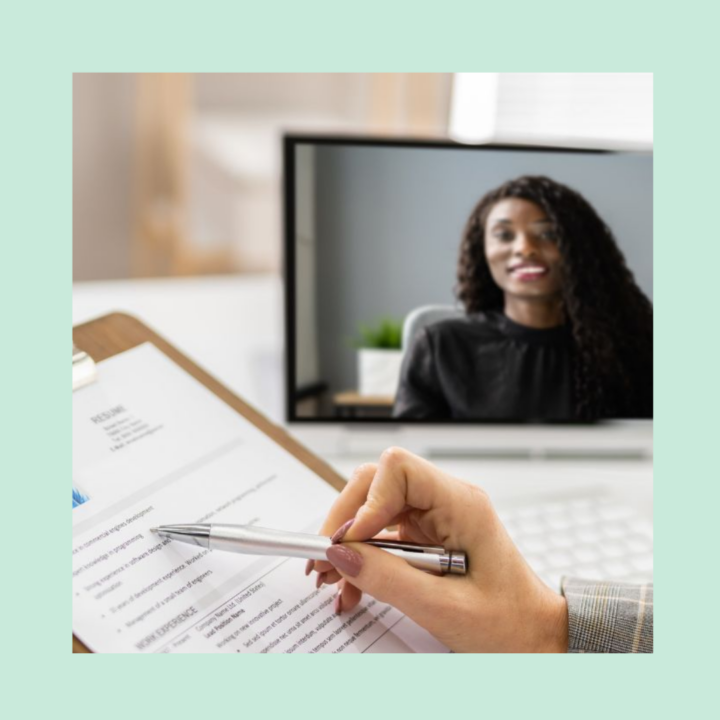 Female hiring manager with a resume, pen and clipboard in her hand conducting a video screening interview on her laptop with an African American female dressed in a black blouse