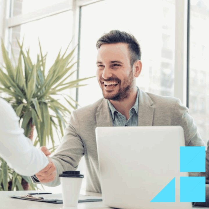 Two good interviewers dressed professional sitting at a desk behind a white laptop shaking the hand of a female job candidate in a white blouse